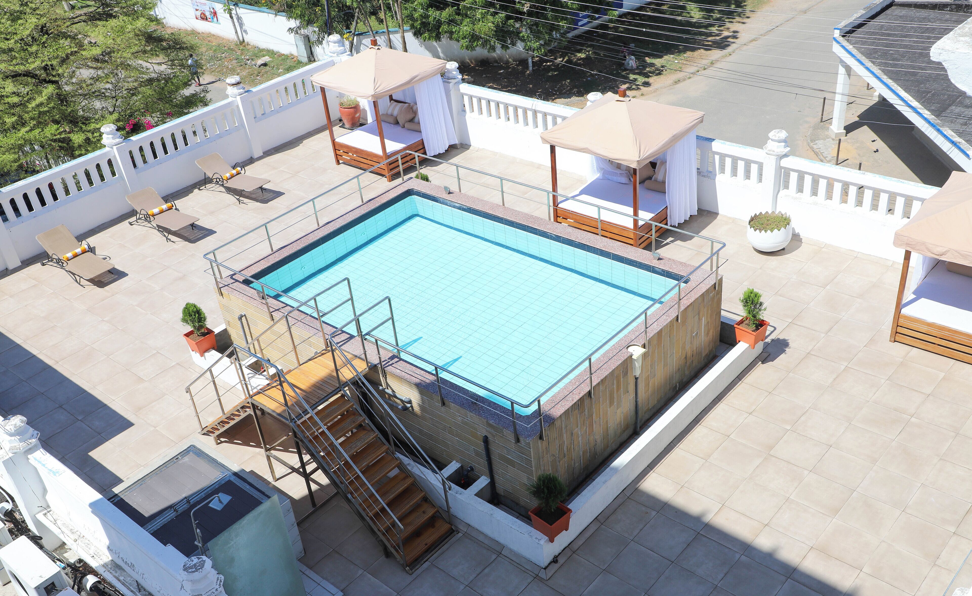 Une piscine sur le toit, avec une terrasse en bois, un petit escalier et quelques chaises longues.