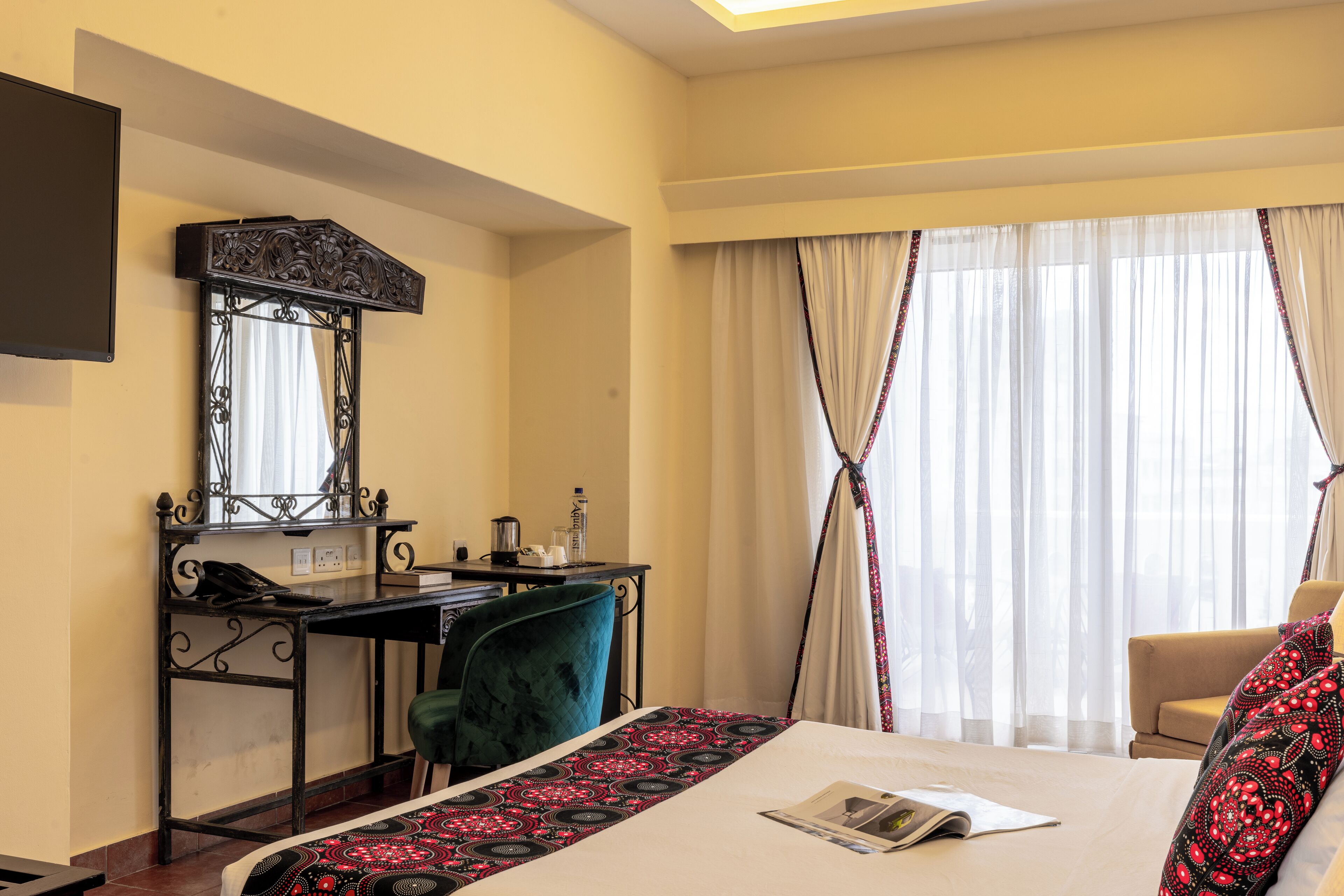 Ein Hotelzimmer mit Bett, Schreibtisch, Stuhl, Spiegel und einem Fenster mit Vorhängen.