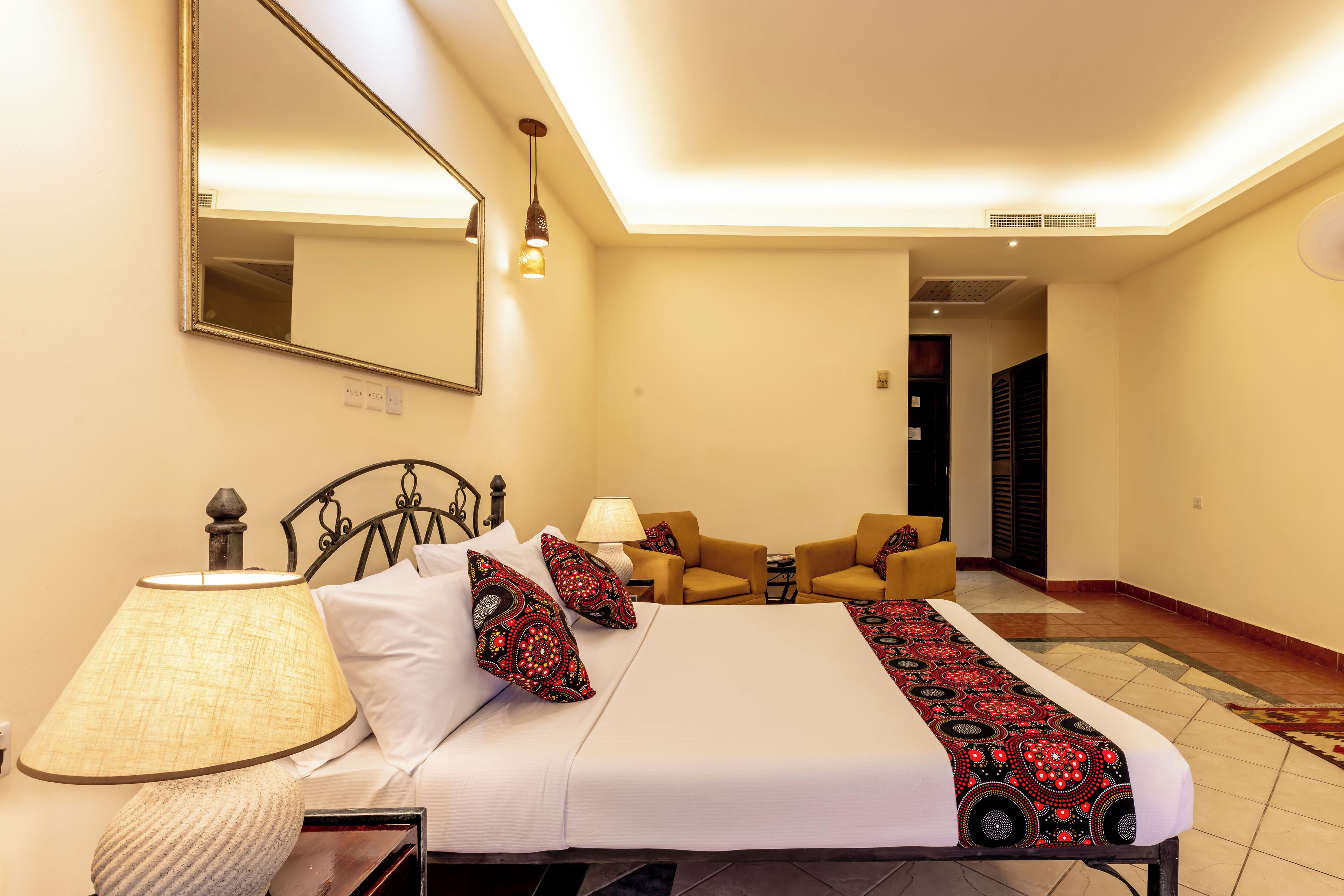 A hotel room with a bed, two armchairs, a table, a lamp, and a mirror.
