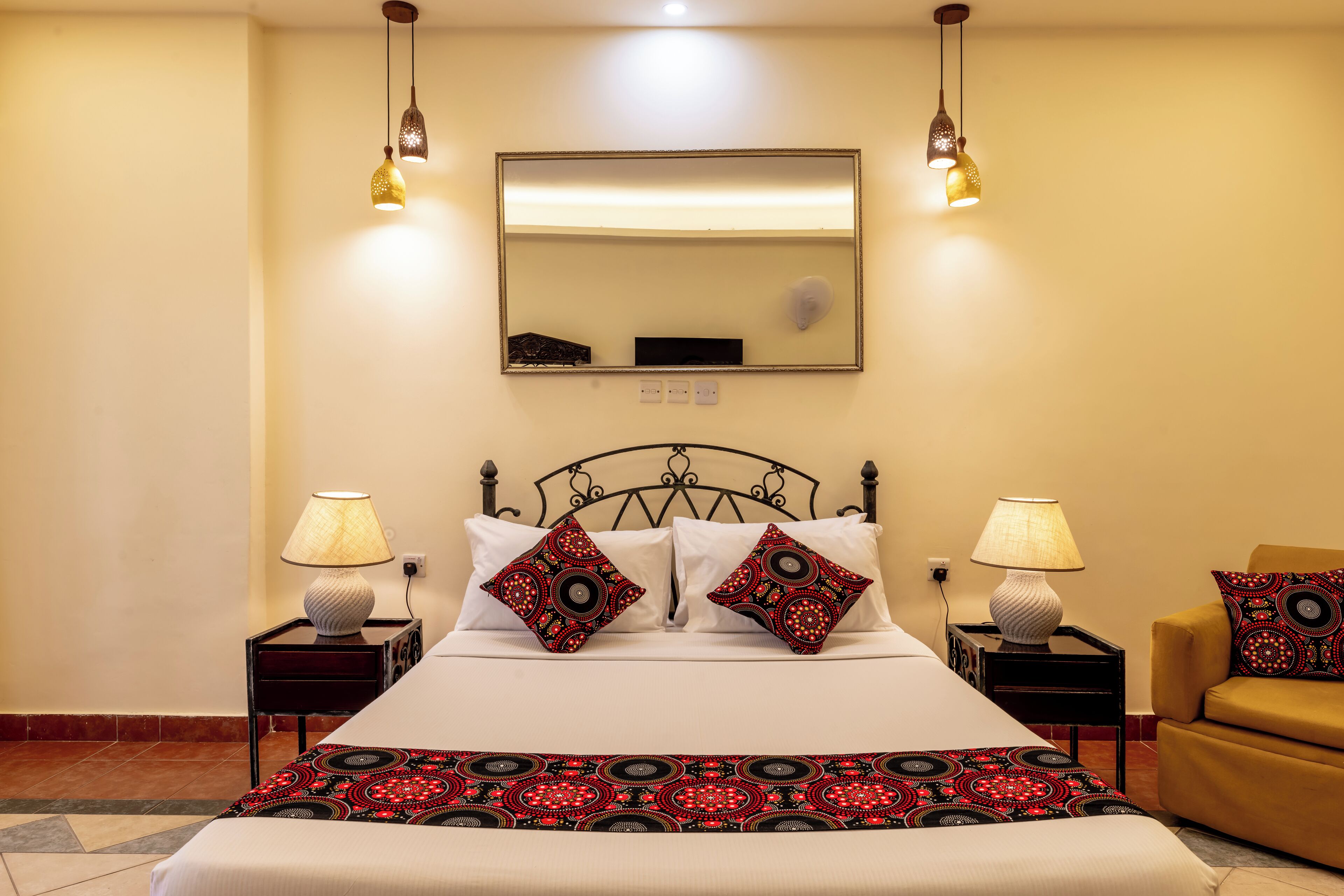 Una cama bien hecha con dos almohadones decorativos, una lámpara de noche y una silla.