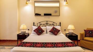 Una cama bien hecha con dos almohadones decorativos, una lámpara de noche y una silla.