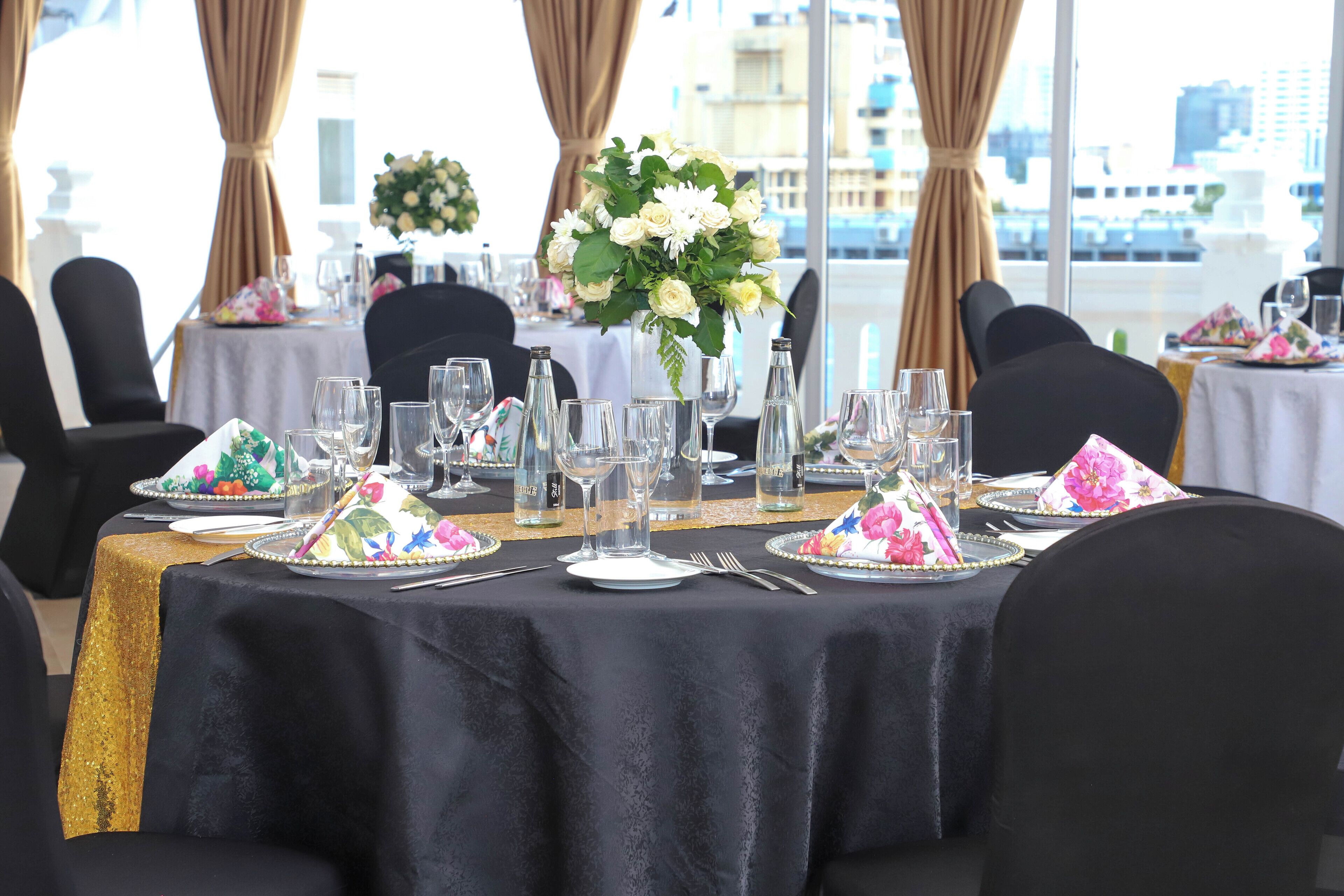 A table set for a formal event with a black tablecloth, white plates, clear glasses, and a floral centerpiece.