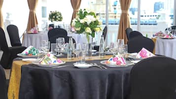 Mesa dispuesta para un evento formal, con mantel negro, platos blancos, vasos transparentes y un centro de mesa floral.