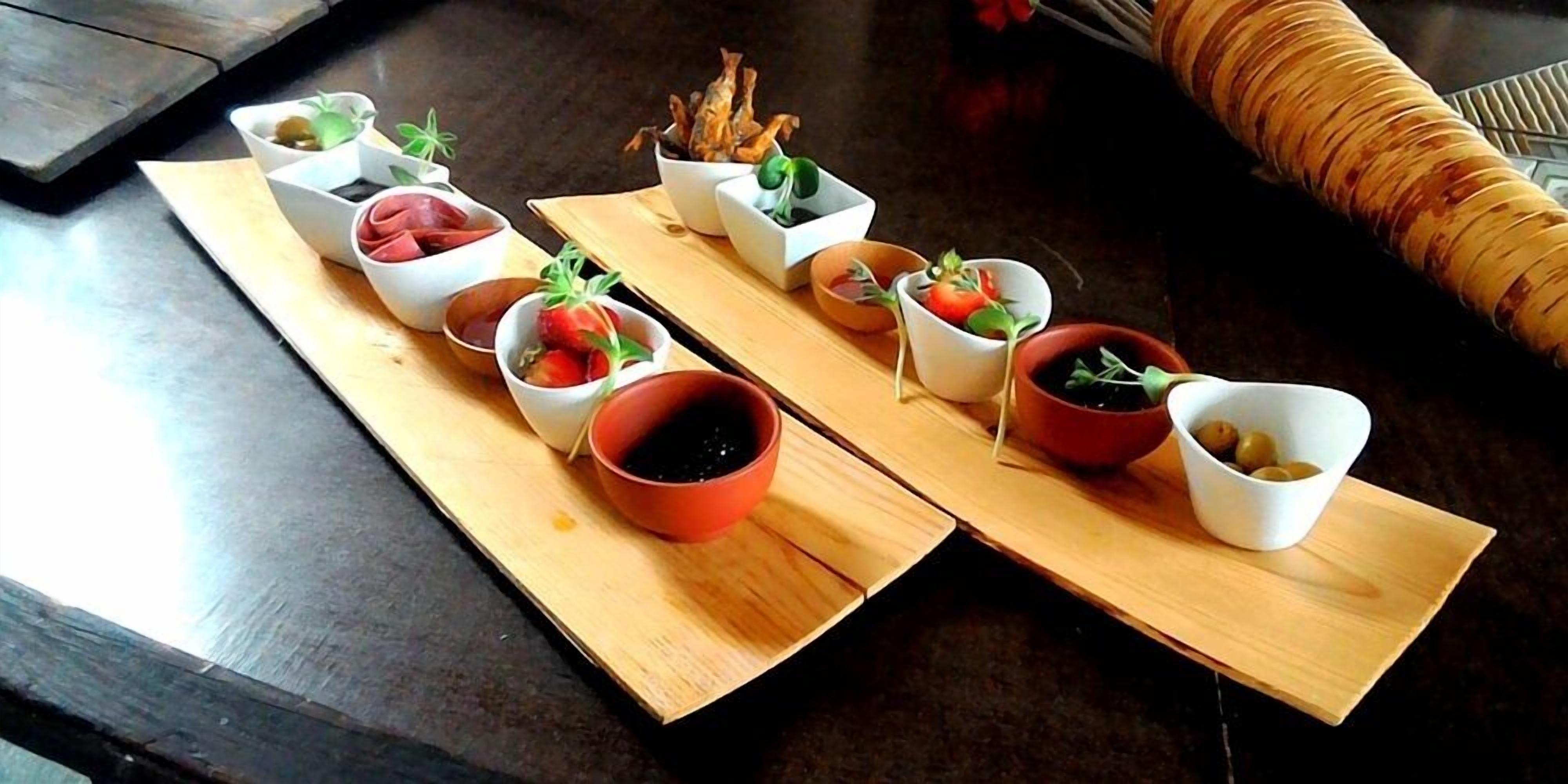 A wooden serving board with various small dishes containing food items and herbs.