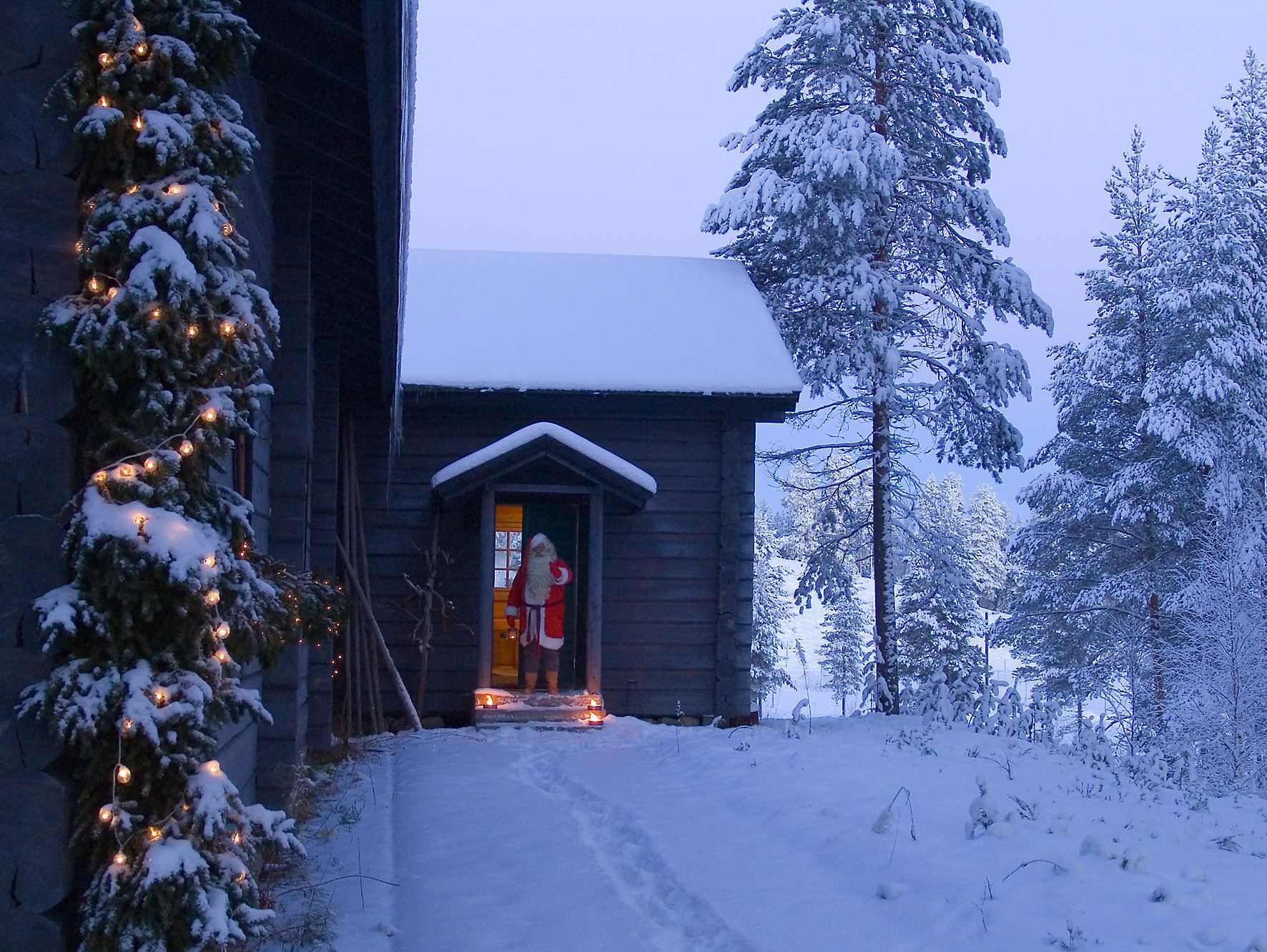 A wooden cabin with a snow-covered roof and a lit doorway.