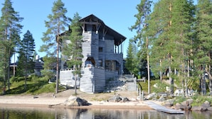 Une cabane en bois dotée d’un balcon, située au bord d’un lac entouré d’arbres.