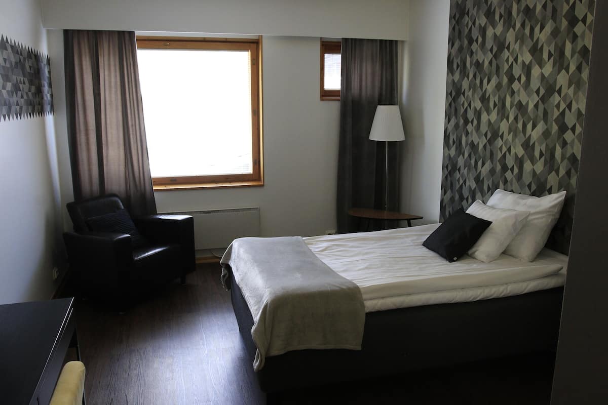 Una habitación de hotel con una cama, una silla, una lámpara y una ventana.
