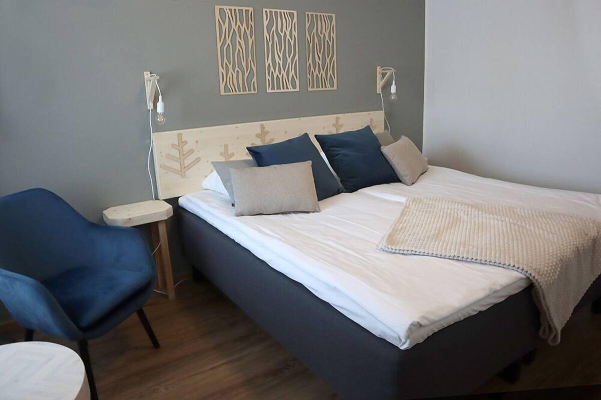 Un dormitorio con cama, una silla, una mesita de noche y decoración en la pared.