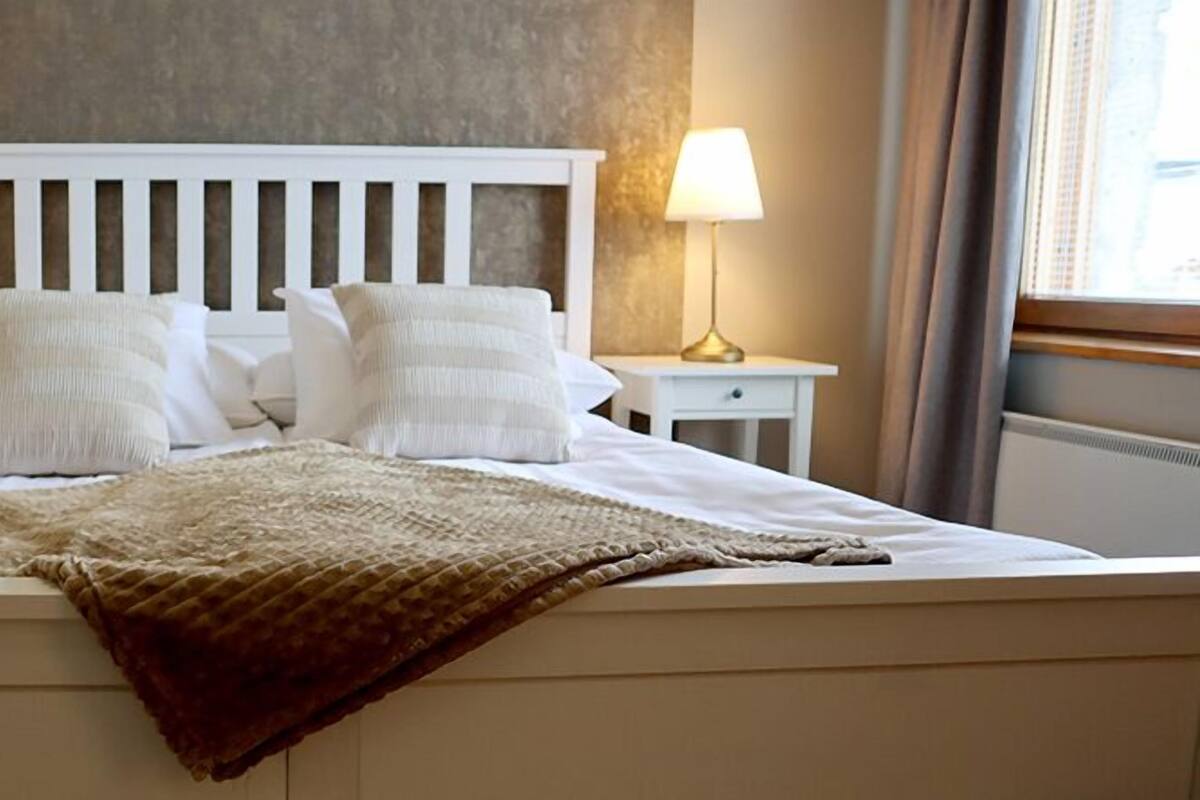 Una cama bien hecha con sábanas blancas y dos almohadas, flanqueada por mesitas de noche con lámparas.