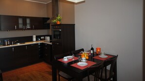 A modern kitchen with dark cabinetry, a central island, and a dining area with red placemats and chairs. - Apartament Nadmorski Sopot 2 (Sopot)