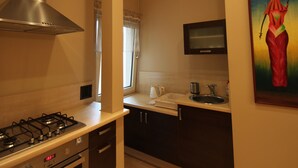 A modern kitchen with a gas stove, oven, and stainless steel range hood. There is a sink and a microwave above it. The kitchen has dark wooden cabinets and a tiled floor. - Apartament Nadmorski Sopot 2 (Sopot)