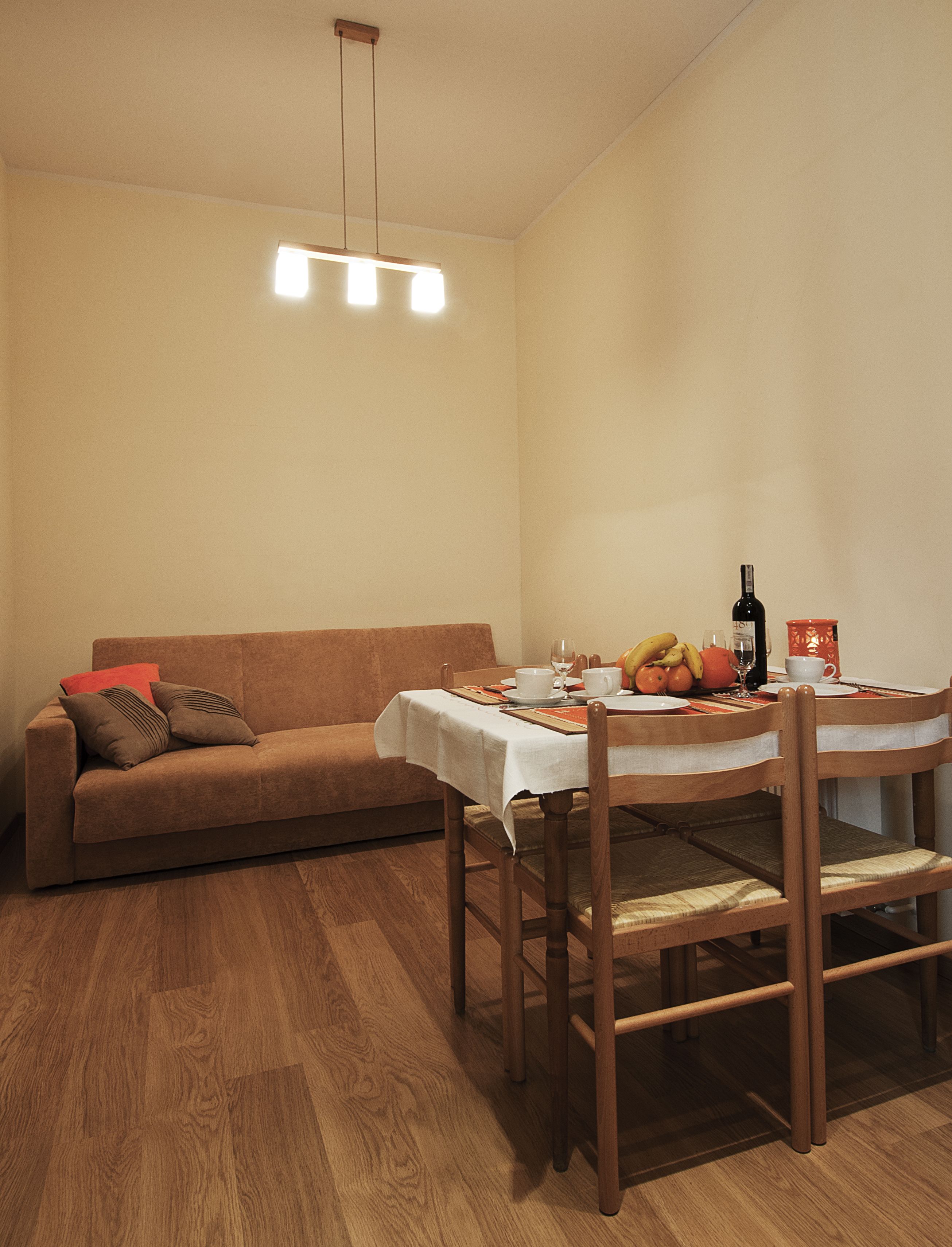 A dining area with a wooden table set for two, a brown sofa, and a ceiling light fixture.