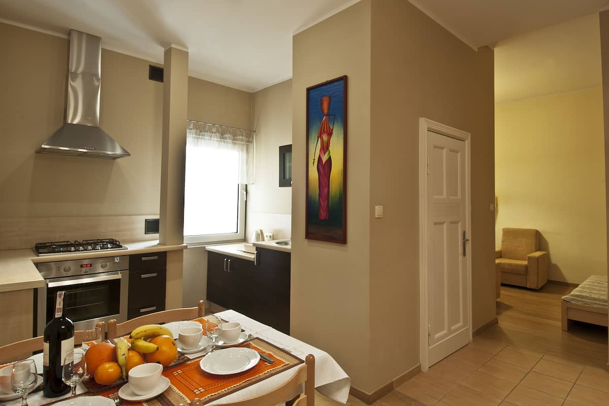 A modern kitchen with a dining area, a painting on the wall, and a small seating area with a chair and a sofa.