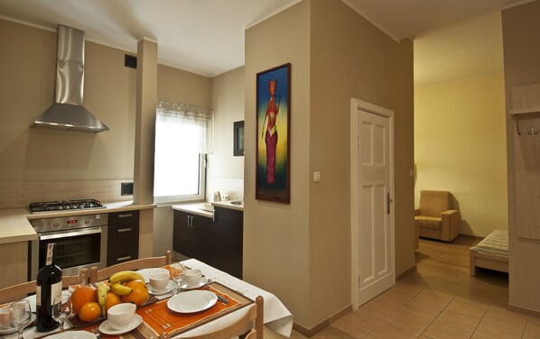 A modern kitchen with a dining area, a painting on the wall, and a small seating area with a chair and a sofa.