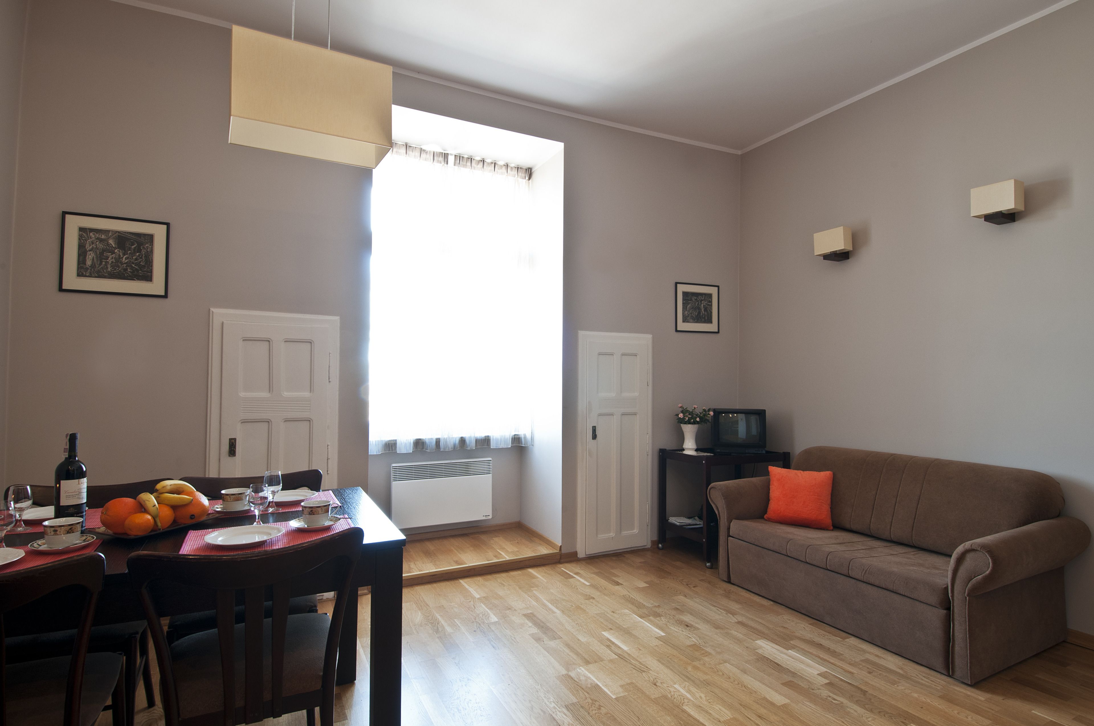 A dining area with a table set for two, a brown sofa, and a window with curtains.