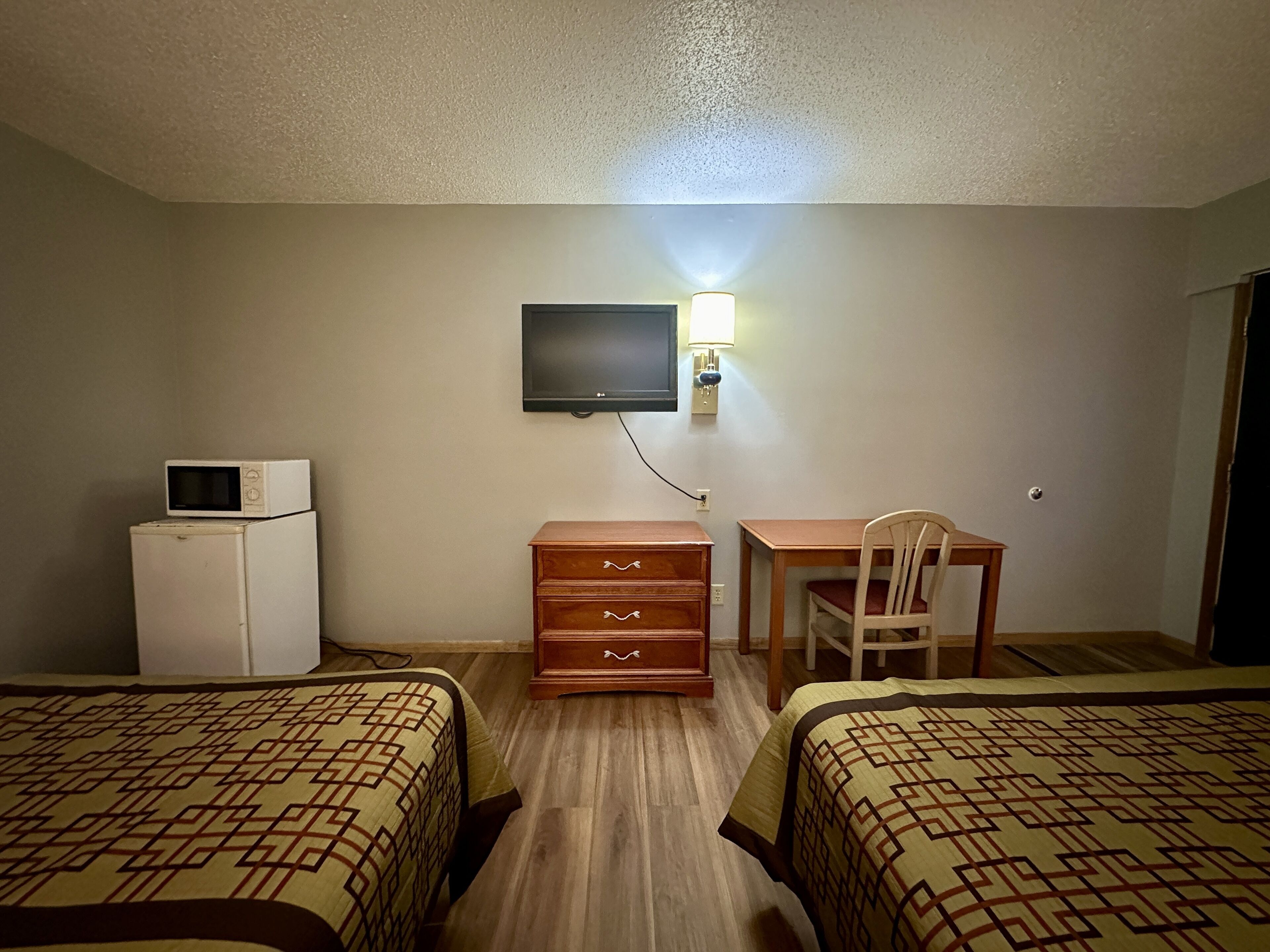 A hotel room with two beds, a desk, a chair, a TV mounted on the wall, and a microwave on the dresser.