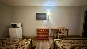 A hotel room with two beds, a desk, a chair, a TV mounted on the wall, and a microwave on the dresser.