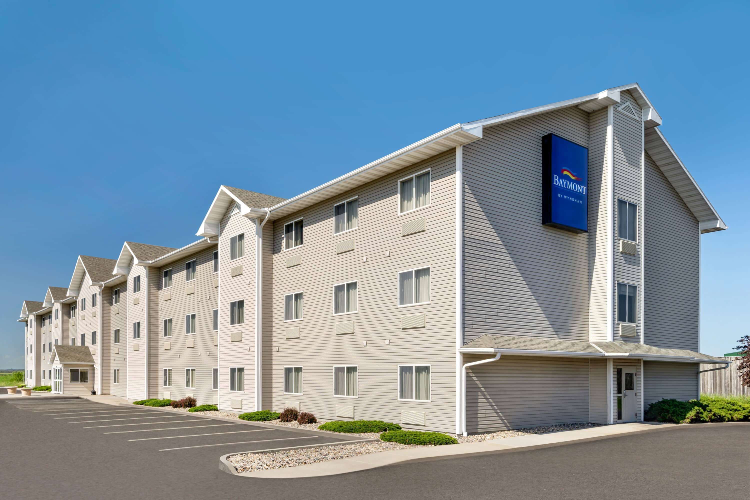 Un hotel de varios pisos con un llamativo letrero de Baymont, un estacionamiento y un exterior bien cuidado.