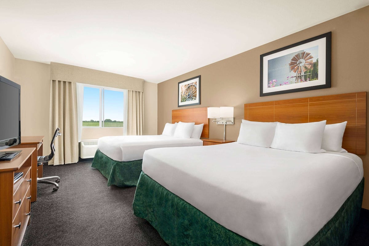 A hotel room with two beds, a desk, a chair, and a TV.