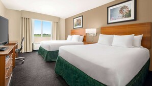 A hotel room with two beds, a desk, a chair, and a TV.