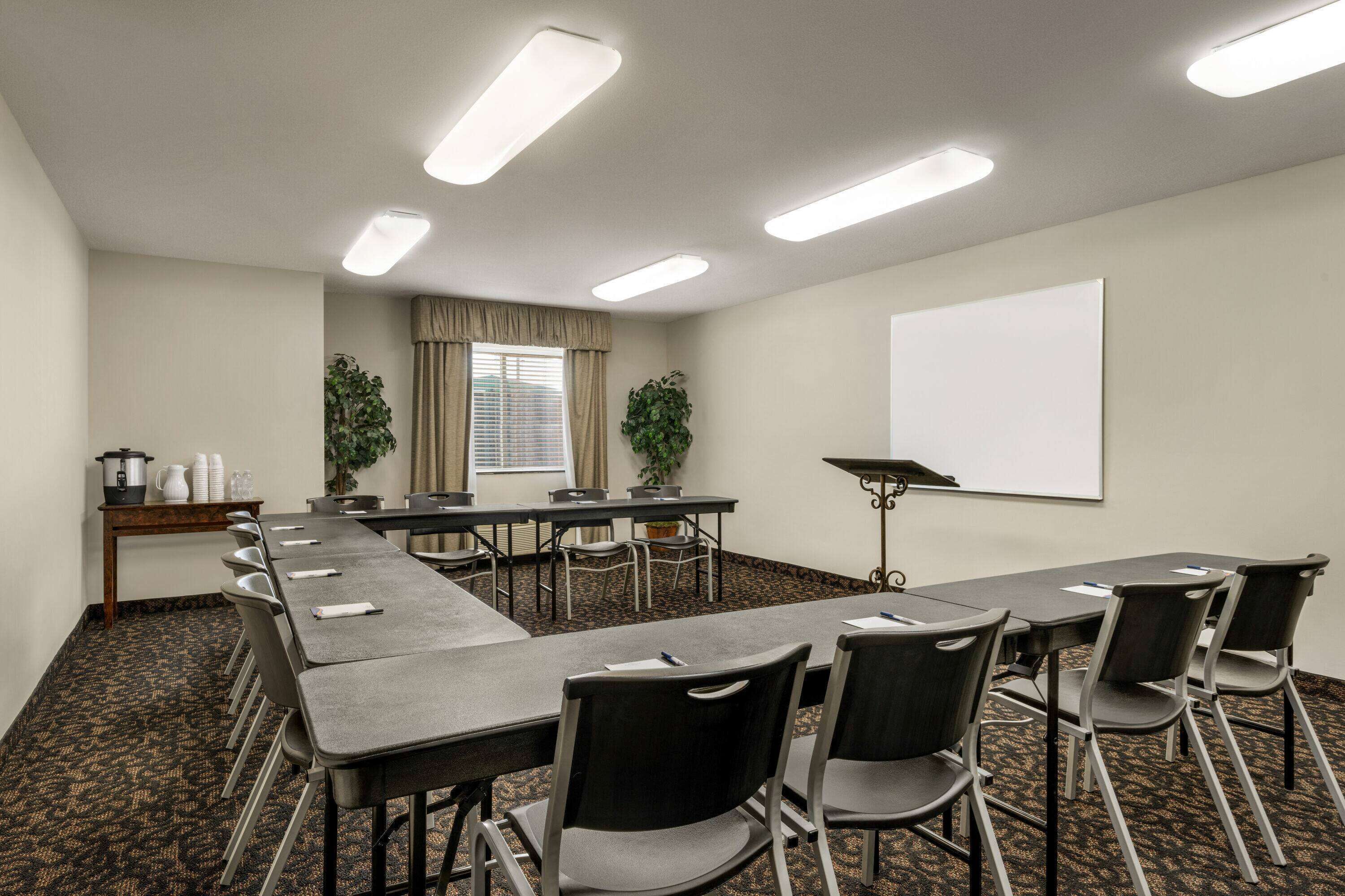 Sala de conferência com uma mesa comprida, cadeiras, tela de projetor e janela com cortinas.