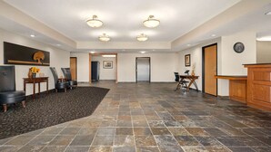 A spacious lobby with a tiled floor, a reception desk, and a seating area with chairs and a table.