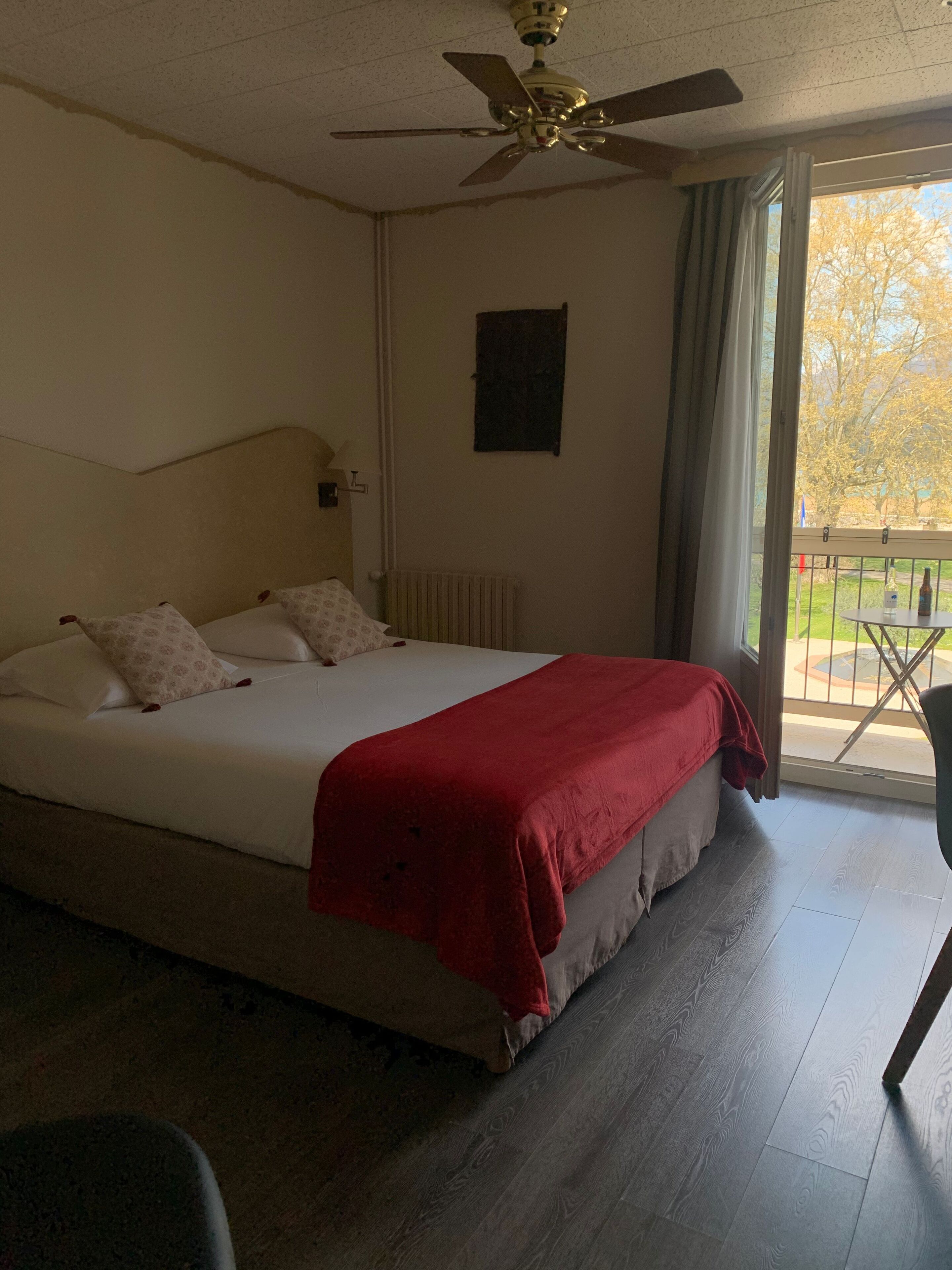 Un dormitorio con cama, ventilador de techo, radiador y vistas al exterior a través de una ventana.