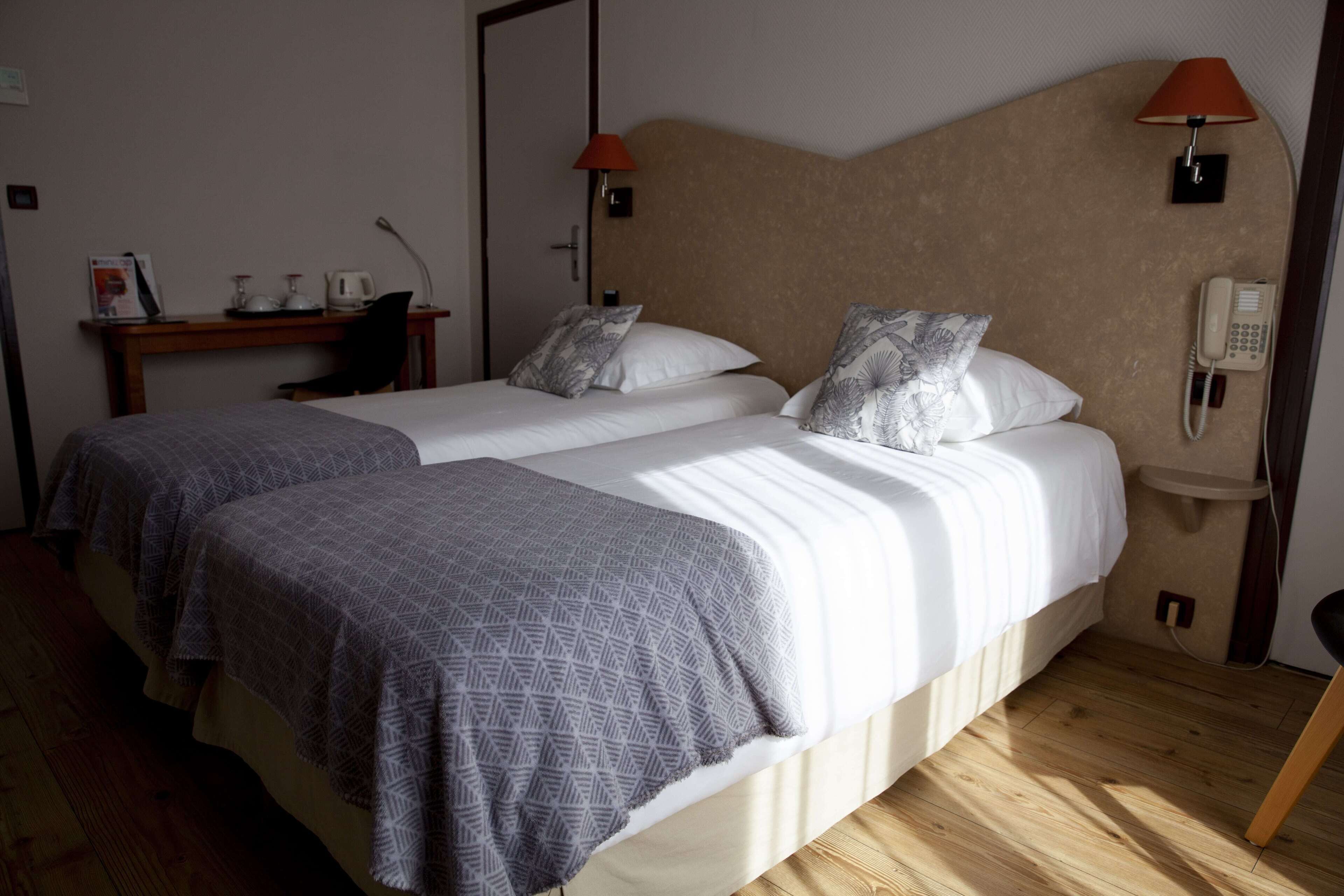 Habitación de hotel con dos camas, un escritorio, una silla, un teléfono y una lámpara.