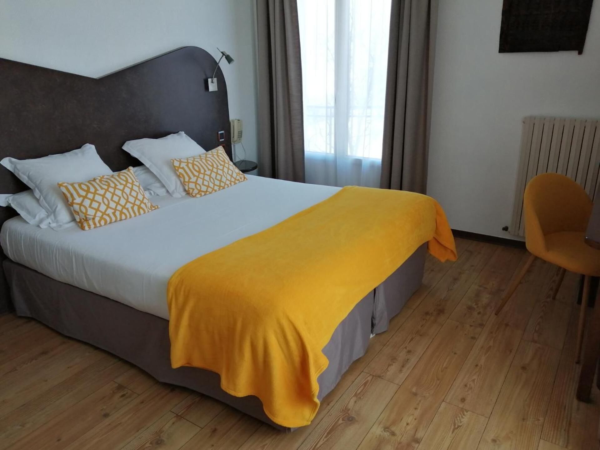 Una habitación de hotel con cama, una silla y una ventana con cortinas.