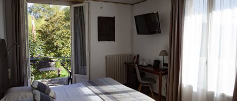 A bedroom with a bed, a desk, a chair, a television, and a balcony with a table and chairs.