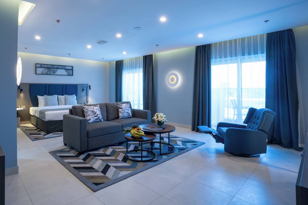 Ein modernes Hotelzimmer mit Bett, Sofa, Sesseln und einem Essbereich mit Tisch und Stühlen.