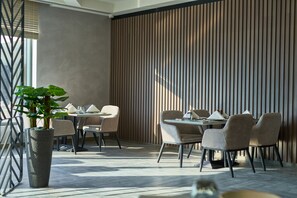 Un espace de salle à manger moderne, agrémenté d’une grande plante en pot, d’une table à manger avec des chaises et d’un mur revêtu de panneaux de bois verticaux.