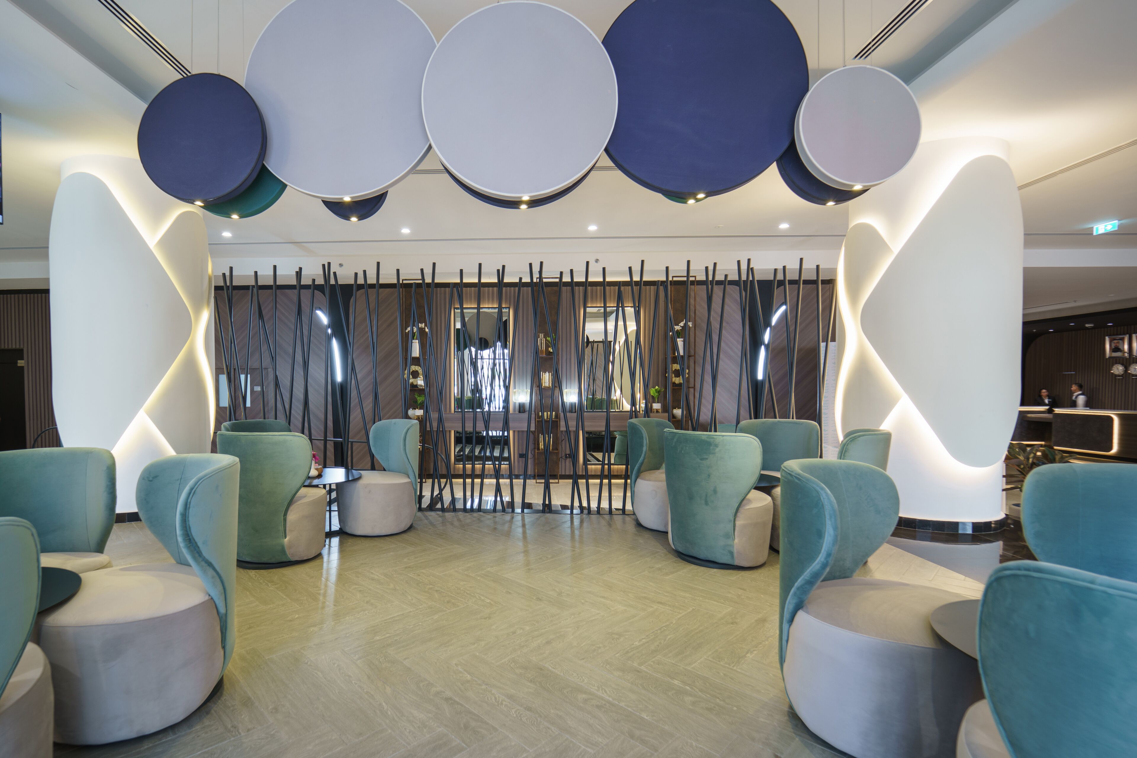 A modern lobby with teal and white seating, a decorative wall, and a reception area in the background.
