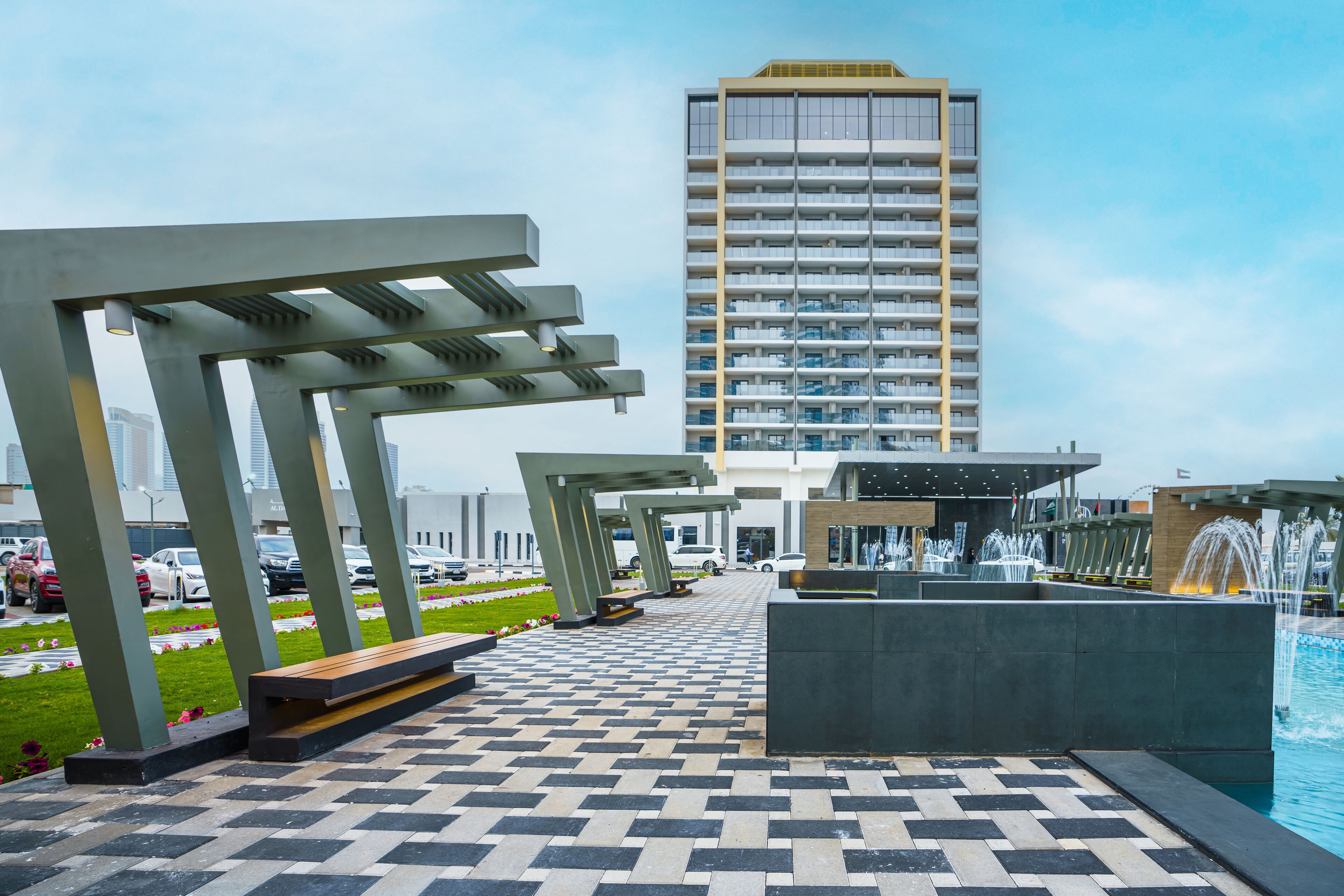 A modern outdoor area with a patterned walkway, benches, a water feature, and a tall building in the background.