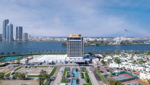 Een hoog hotel met een modern design, gelegen aan een waterkant met uitzicht op de skyline van de stad en een groot reuzenrad op de achtergrond.