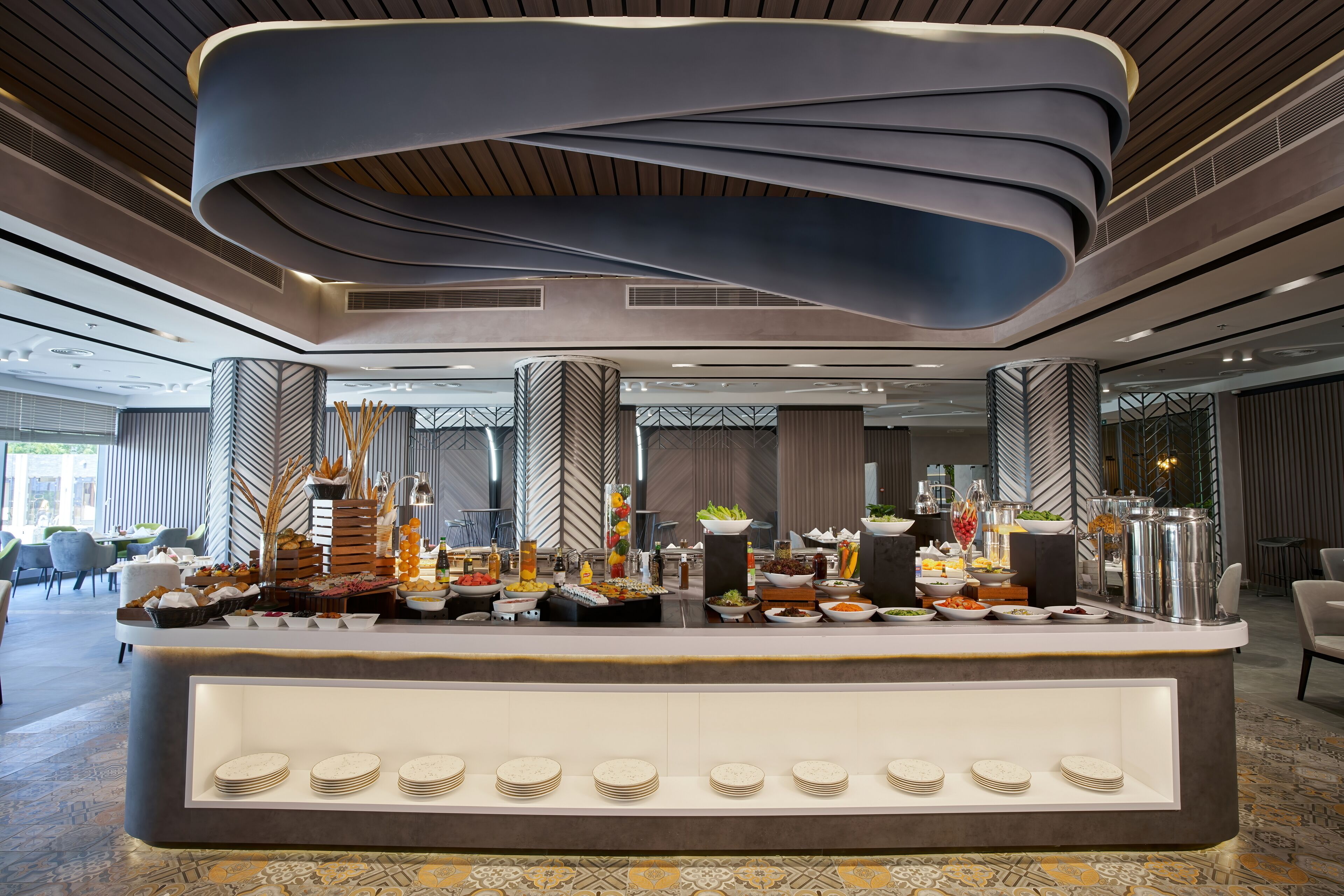 Un moderno hall de hotel con una zona de buffet que ofrece diversas opciones de comida y bebida, un diseño de techo elegante y un suelo estampado.