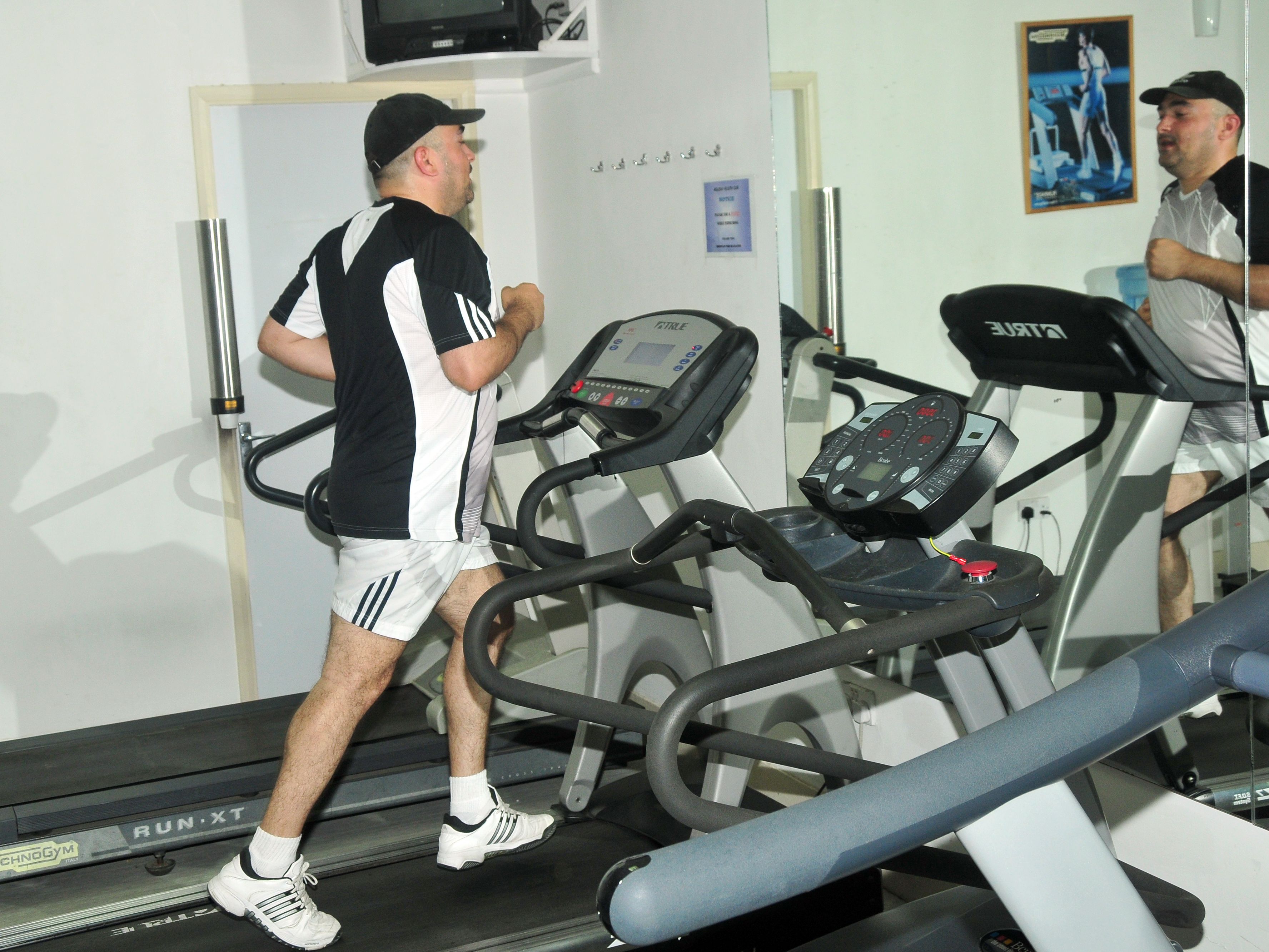 Et fitnessrum med løbebånd og et spejl.