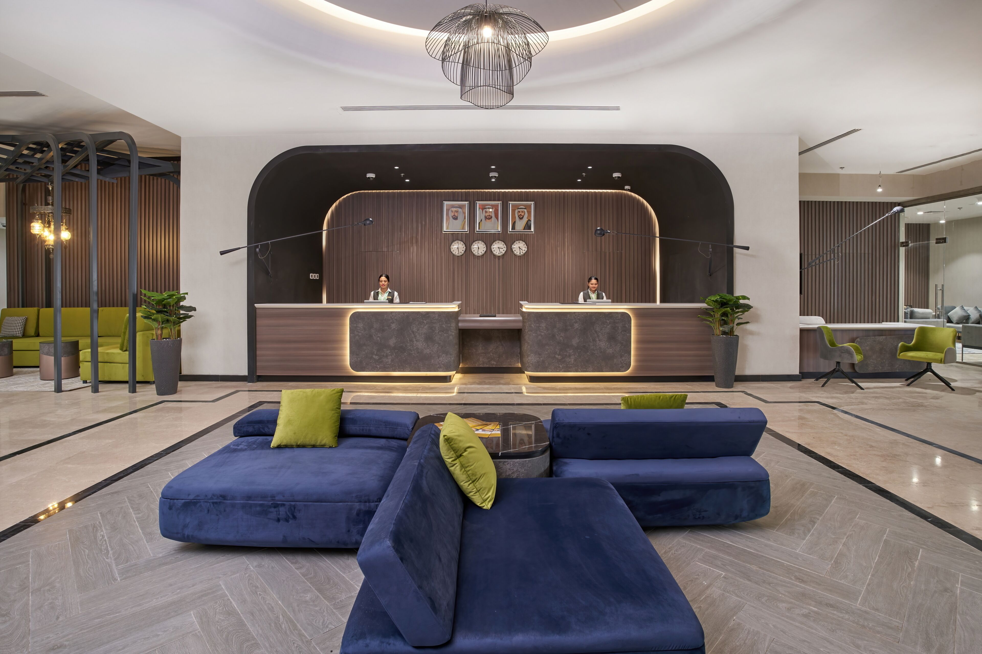Un espace d’accueil moderne avec un comptoir incurvé, deux réceptionnistes et un coin salon doté de canapés bleus et de coussins verts.