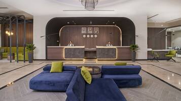 Un espace d’accueil moderne avec un comptoir incurvé, deux réceptionnistes et un coin salon doté de canapés bleus et de coussins verts.