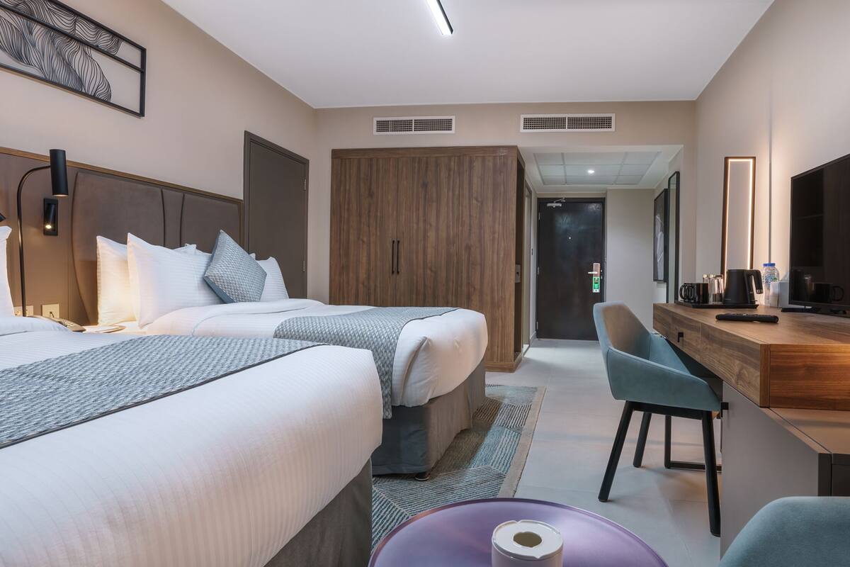 Ein Hotelzimmer mit zwei Betten, einem Schreibtisch mit Computer, einem Fernseher und einer Badezimmertür.