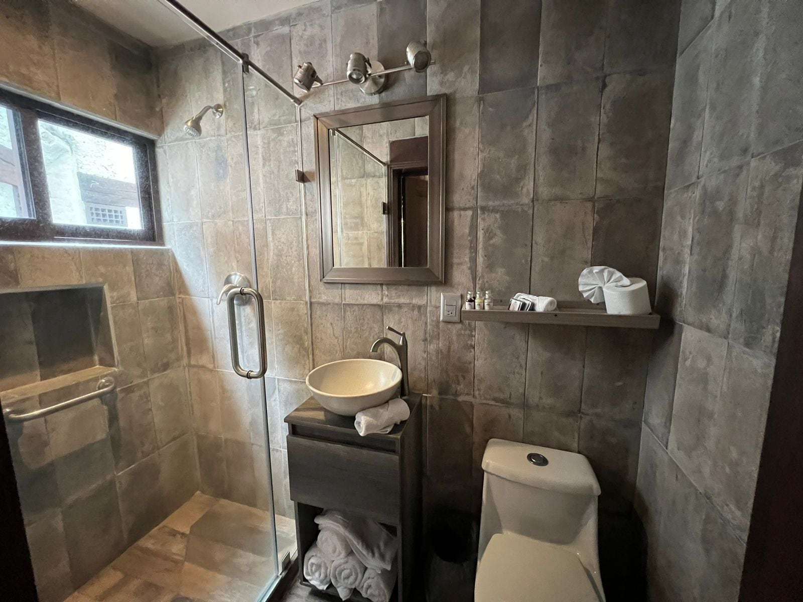 Un baño moderno con ducha envuelta en vidrio, tocador con lavamanos, inodoro y espejo sobre el lavamanos.