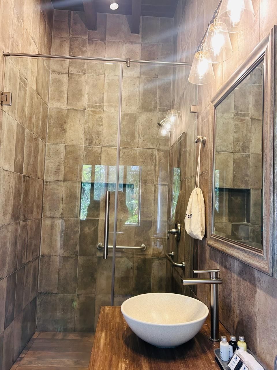 Un baño moderno con un espejo grande, un lavabo sobre encimera y una zona de ducha con mampara de cristal.