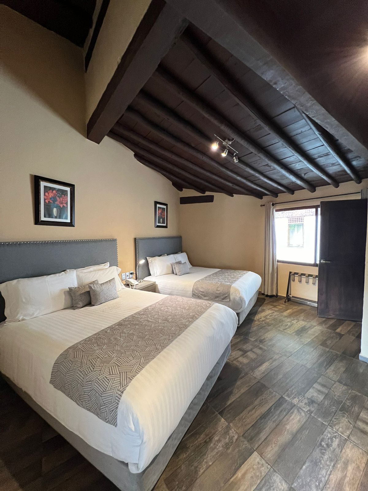 Une chambre d’hôtel avec deux lits, un plancher en bois, un plafond sombre et une fenêtre avec des rideaux.
