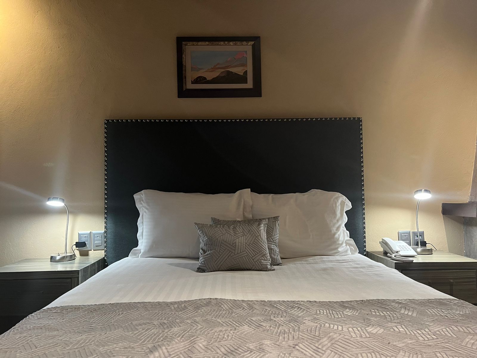 Ein Hotelzimmer mit einem großen Bett, zwei Nachttischlampen, einem gerahmten Bild an der Wand und einem Telefon auf dem Nachttisch.