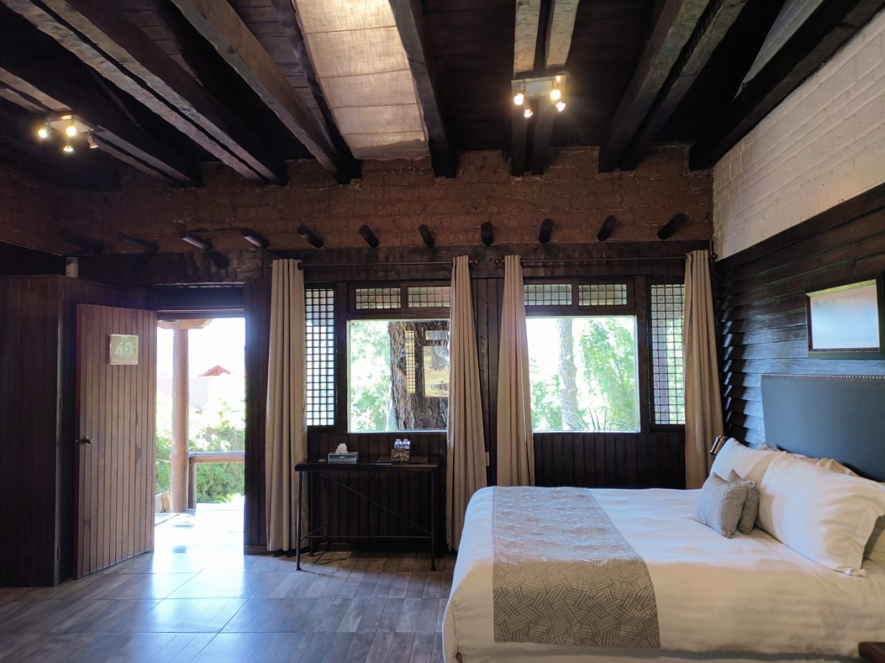 A bedroom with a bed, a desk, and a view of the outdoors.