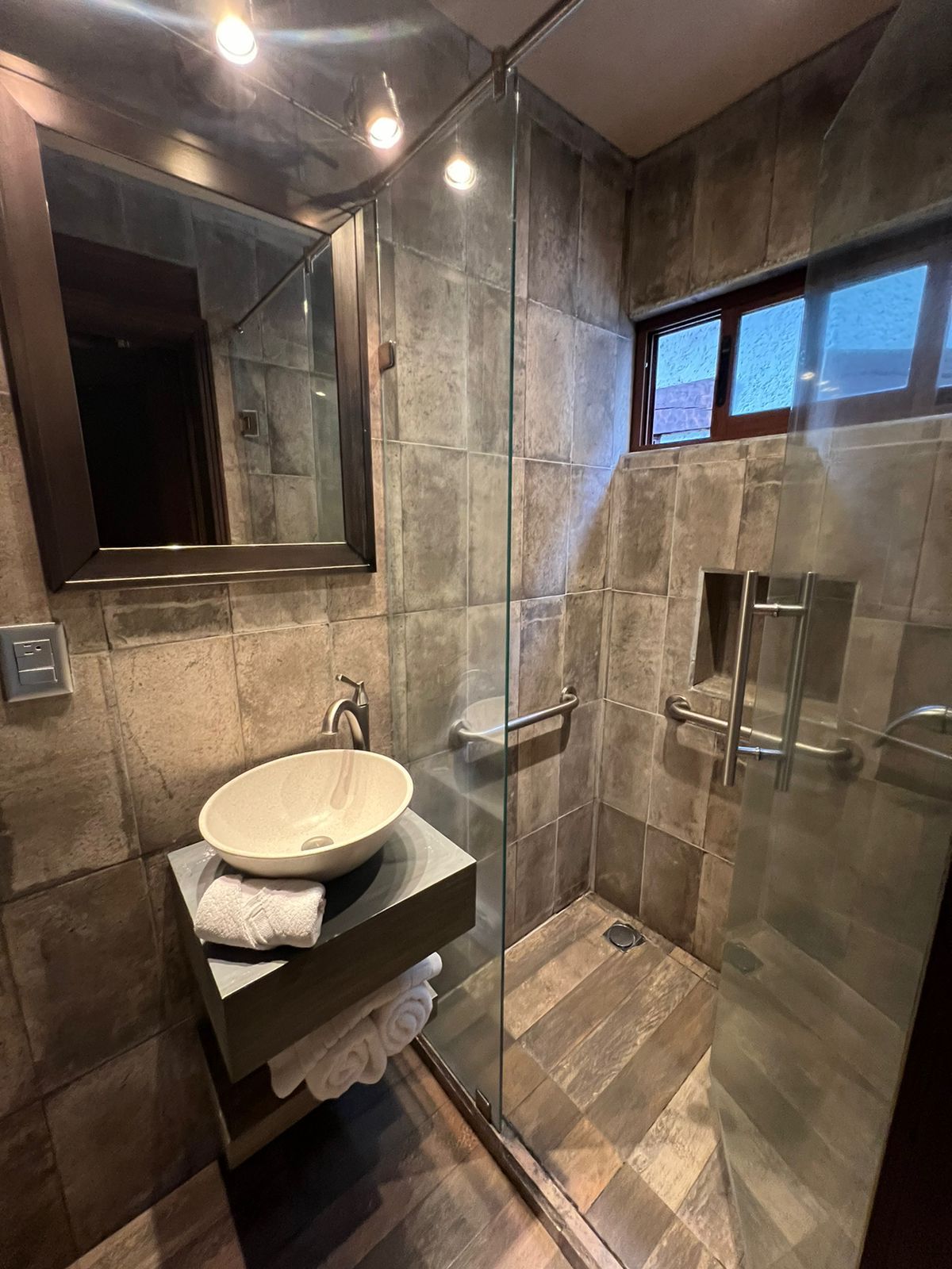 Un baño moderno con ducha de vidrio, un espejo grande y un lavamanos empotrado con toallero.