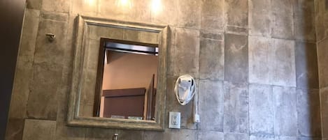 A bathroom with a stone wall, a sink with a vessel basin, a mirror, a towel rack, and a toilet.