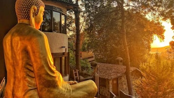 A Buddha statue in a seated position with a view of a sunset and trees in the background.