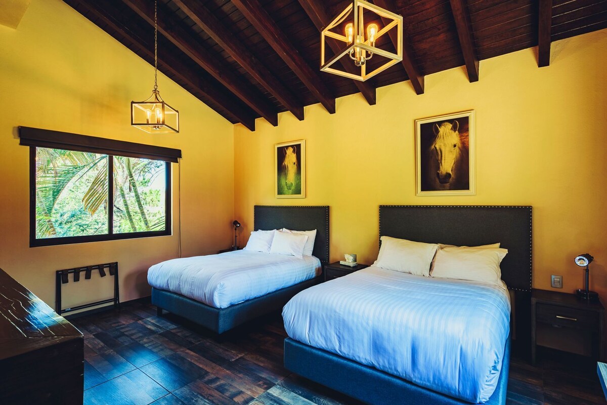 A room with two beds, a window with a view of trees, and a wooden ceiling.