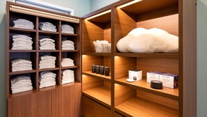 Une armoire en bois avec plusieurs étagères, dont certaines servent à ranger des vêtements pliés et d’autres contiennent des boîtes et un petit appareil électroménager.